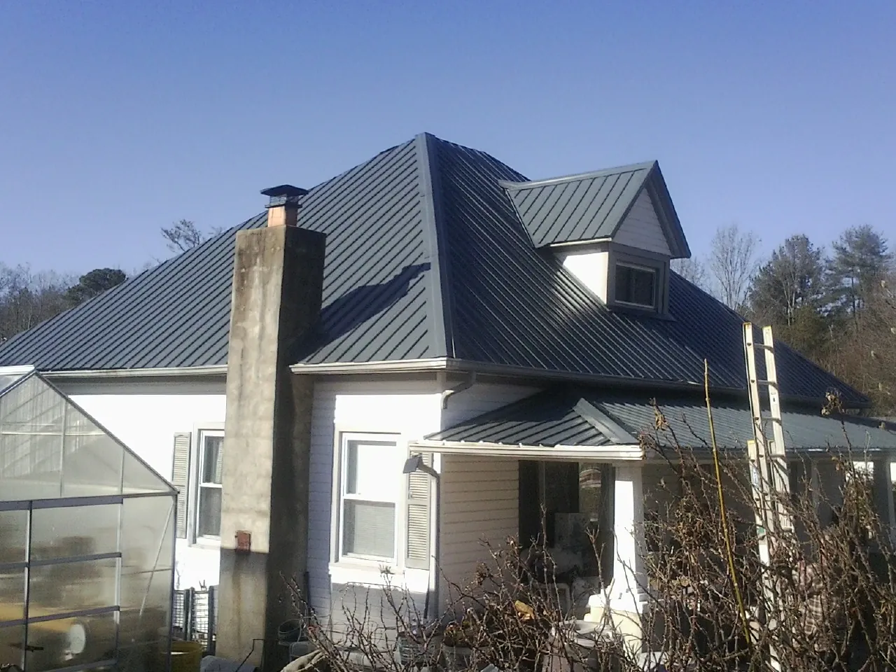 Dark blue standing seam metal roof on a white farmhouse with dormer — Slate & Tile Roof Repair by Roofing Brothers in North Lawrence