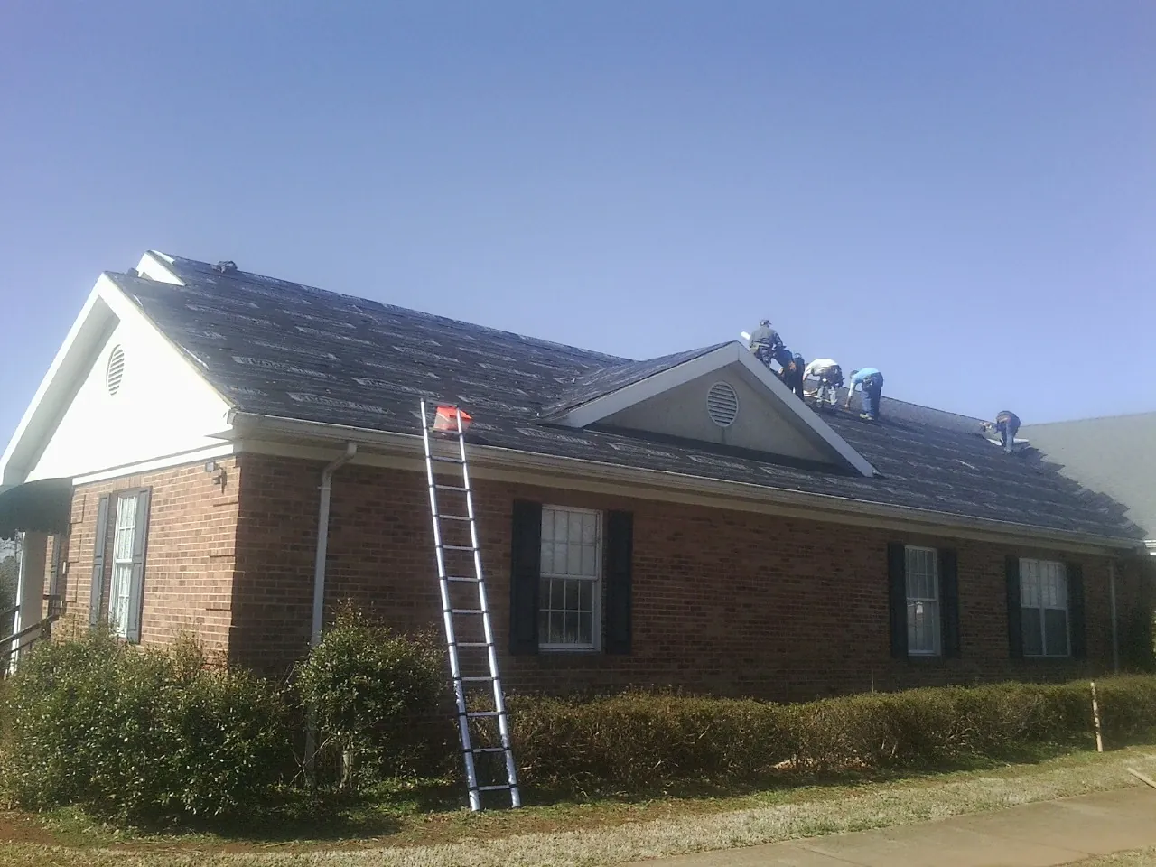 Crew tearing shingles off a brick ranch roof with a ladder set — Metal Roof Repair work by our crew in North Lawrence