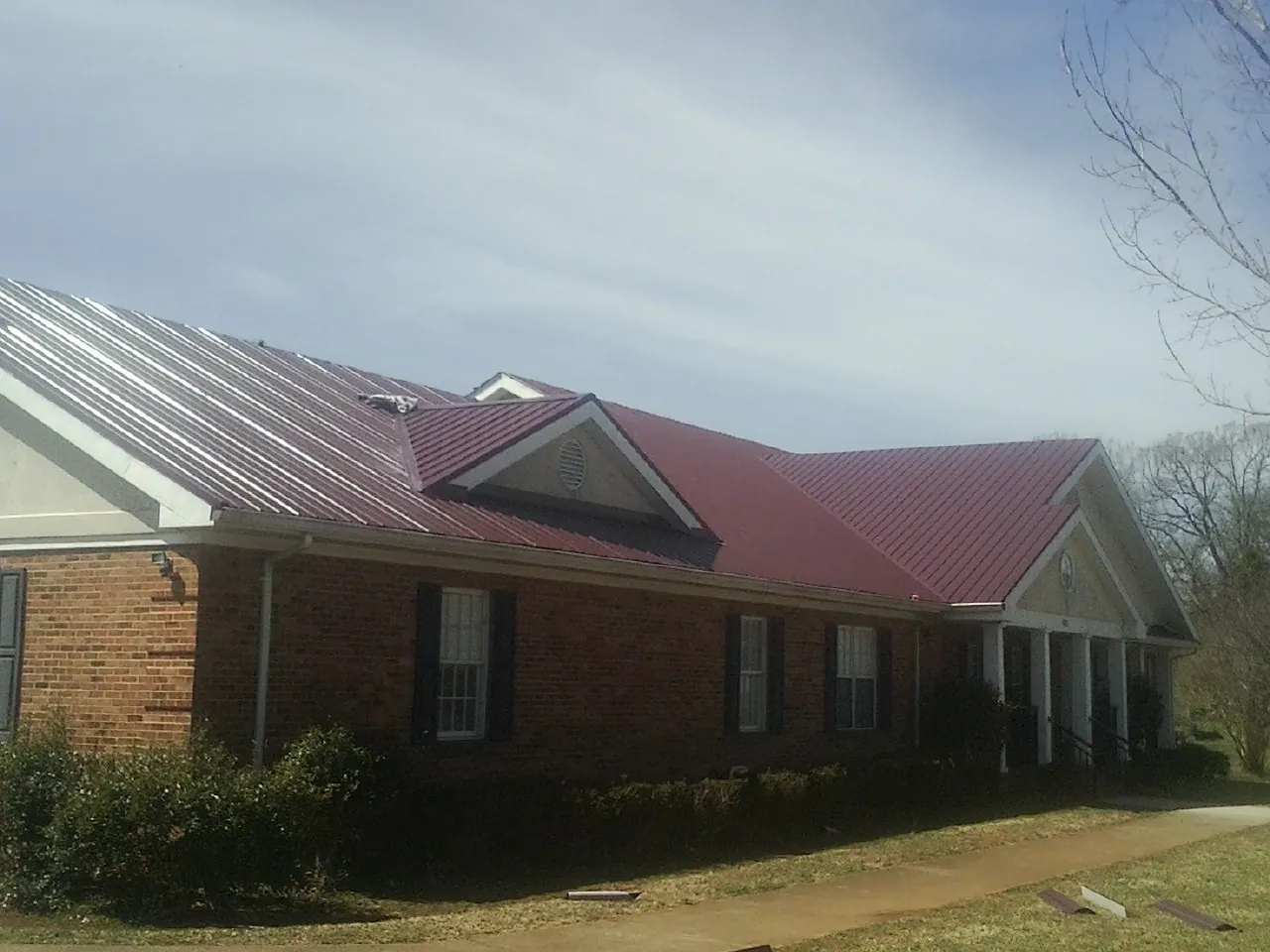 Red metal roof with gabled entries on a long brick building, from a Hail Damage Roof Repair job in North Lawrence