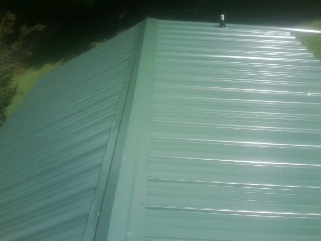 New green metal panels meeting at the ridge of a roof — Flat Roof Repair work by our crew in North Lawrence