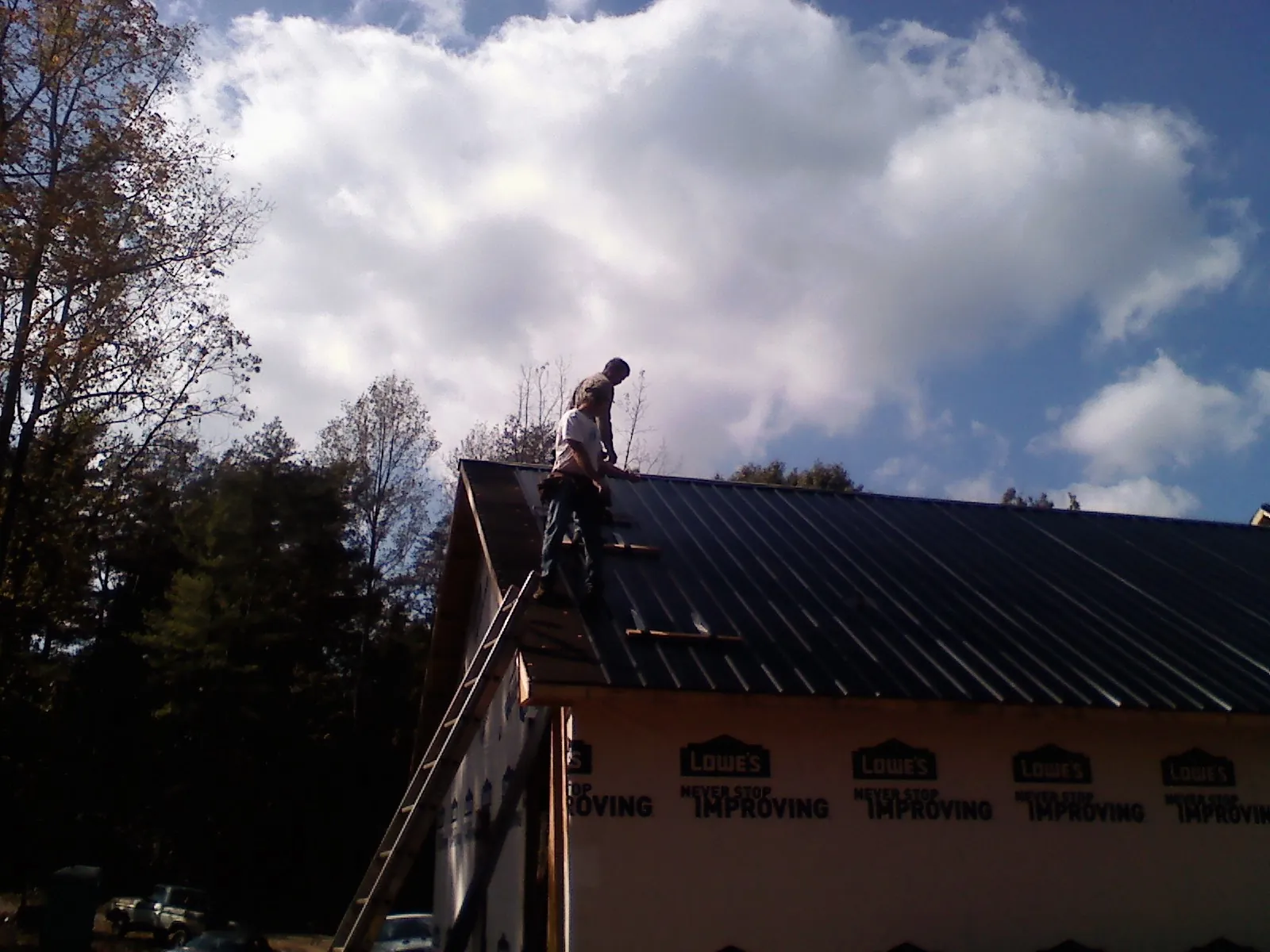 Roofer fastening dark metal panels high against a cloudy sky, from a Roof Inspection job in North Lawrence