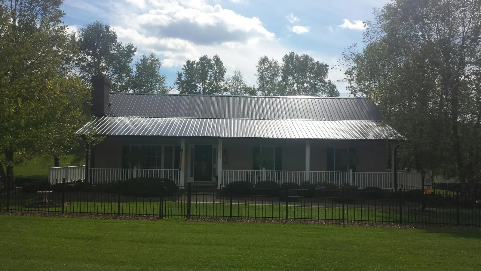 Gray metal roof on a brick ranch with a full width front porch — Gutter Guard Installation work by our crew in North Lawrence