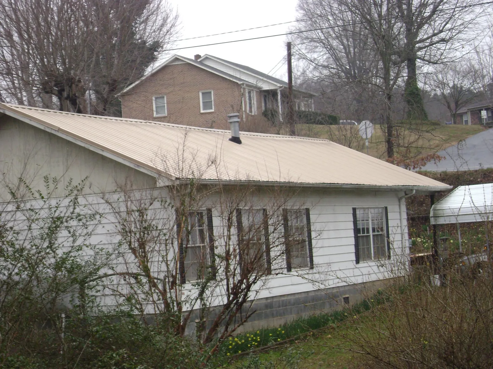 Tan metal roof on a white sided house set into a hillside — Commercial Roofing by Roofing Brothers in North Lawrence