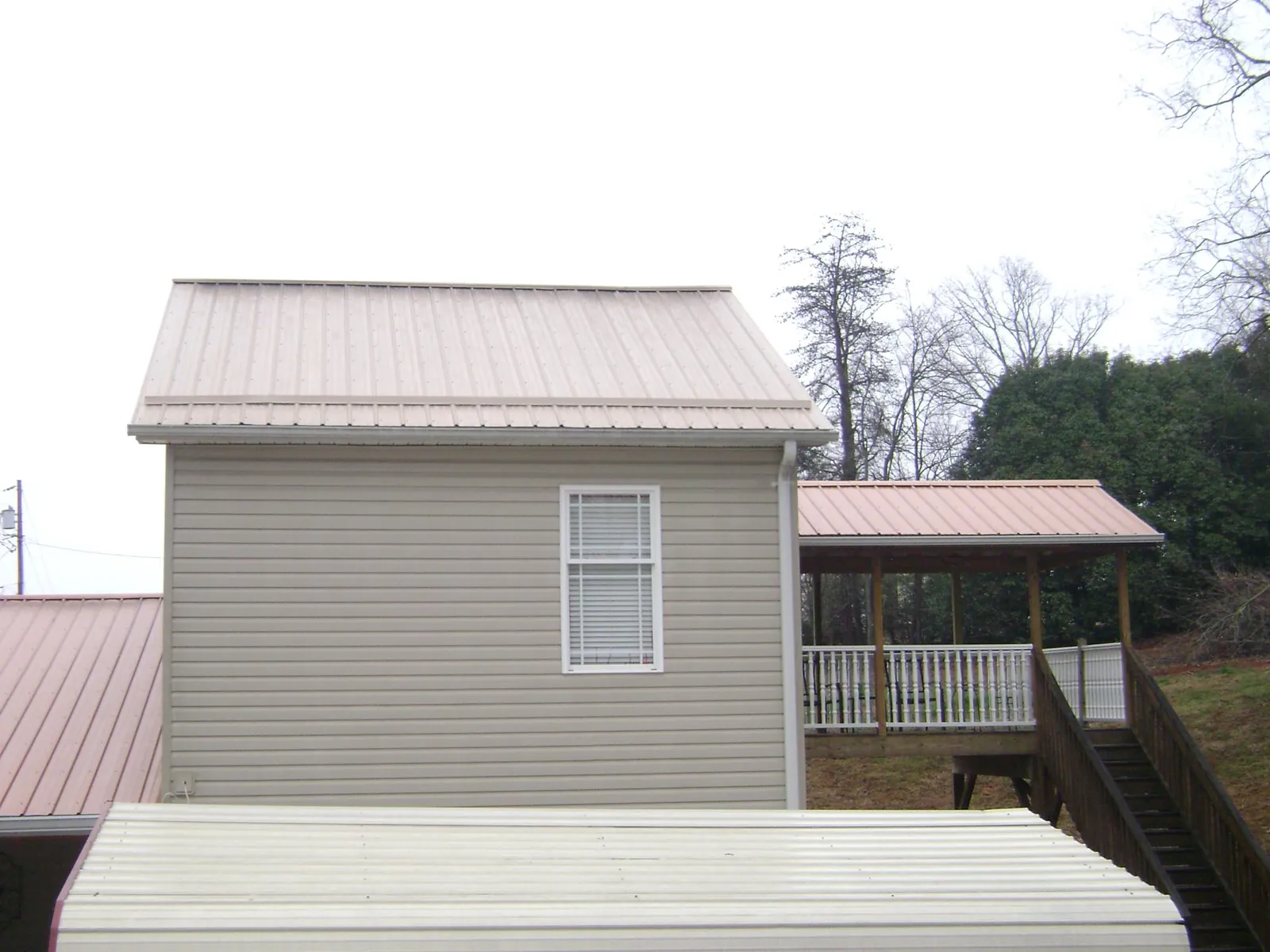 Tan metal roofs on a two story addition and attached porch, from a Roof Replacement job in North Lawrence